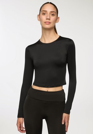 Crop top nero a maniche lunghe con una texture liscia e scollatura rotonda, abbinato a leggings neri a vita alta.