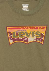Zelena Levi's majica s višebojnim logotipom koji prikazuje zalazak sunca, drveće i terensko vozilo.