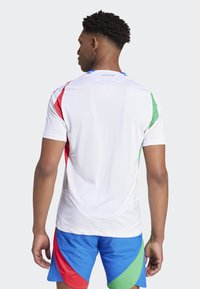 Biele športové tričko s červenými, zelenými a modrými akcentmi na rukávoch, v páre s modrými šortkami. Vyrobené z ľahkej, texturovanej látky.