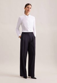 White collared blouse, slim-fit, long sleeves; paired with high-waisted, wide-leg black trousers; sleek texture; pointed black heels.