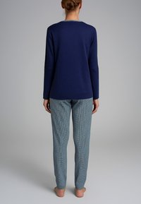Maglietta navy a maniche lunghe con scollatura rotonda, abbinata a pantaloni chiari a fantasia blu. La maglietta è liscia; i pantaloni hanno una trama a scacchi.