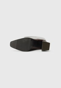 Bottine en cuir marron avec un talon carré et une semelle en caoutchouc texturée, présentant des nervures verticales pour une meilleure adhérence.