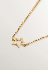 Collar de cadena de oro que presenta un colgante en forma de estrella con un centro abierto. La cadena está compuesta por eslabones ovalados interconectados.