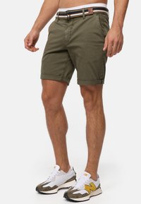 Shorts en coton vert olive avec des ourlets retroussés, comportant une ceinture rayée multicolore avec un accent en cuir marron. Coupe décontractée, texture solide.