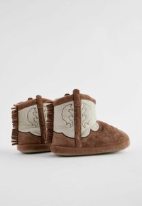 Braune Plüschstiefel mit einem cremefarbenen Stoffpanel, fransigen Details und einer weichen Sohle. Das Design weist ein genähtes Muster auf, das Wellen ähnelt.