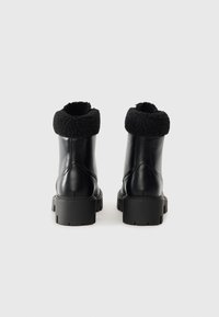 Sorte skinn ankle boots med en strukturert svart fleecekant, tung såle og slankt design. Klare sømmer og synlige hardware-detaljer.