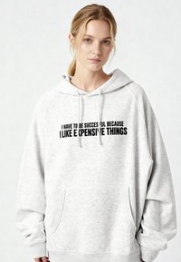 Felpa grigia oversize in tessuto morbido, con tasca frontale e coulisse. Testo nero sul davanti con una frase umoristica.