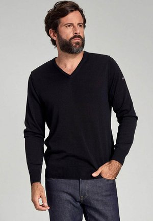 Sort v-hals sweater lavet af strikket stof med lange ærmer og ribbet kant. Bæres med blå jeans, der har et lille logo på ærmet.