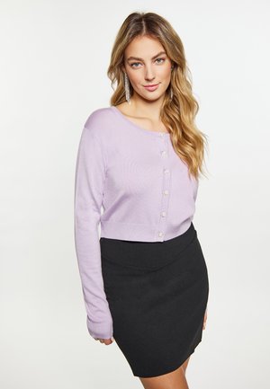 Cardigan scurt de culoare liliac, cu mâneci lungi și închidere cu nasturi, combinat cu o fustă neagră mulată. Textură netedă, design minimalist și strălucire subtilă.