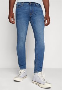 Blå denimjeans med slim fit, som har fem fickor, bältesömmar och ljus sömnad. Matchad med grå höga sneakers.