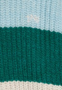 Strikket genser med lyseblå, teal og kremfargede horisontale striper. Har 'TNS' brodert i hvitt på den lyseblå delen. Myk tekstur.
