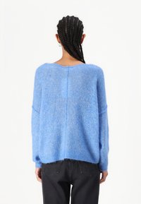 Απαλή μπλε πουλόβερ από φ fluffy ύφασμα. Διαθέτει χαλαρή εφαρμογή, πτώση στους ώμους και φαρδύ ντεκολτέ με κεντρική ραφή.