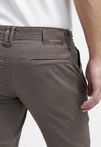 Dunkelgraue Hose mit einem Lederpatch, auf dem "BOSS ORANGE" steht, mit sichtbaren Taschen und einem glatten, strukturierten Stoff.