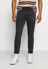 Jeans ajustados gris oscuro con una textura suave y lisa. Con los puños doblados y detalles de costura mínimos. Combinados con zapatillas blancas.