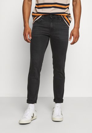 Jeans ajustados gris oscuro con una textura suave y lisa. Con los puños doblados y detalles de costura mínimos. Combinados con zapatillas blancas.