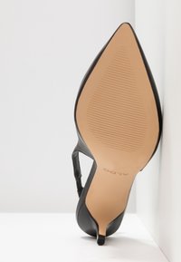 Czarny but na wysokim obcasie z zaostrzonym noskiem, gładką skórzaną cholewką i beżową gumową podeszwą z poziomymi rowkami, prezentowany pod kątem.