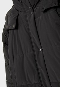 Crna puffer jakna s kapuljačom, koja ima kvadratni dizajn, dugme na kopčanje i glatku, blago sjajnu teksturu. Funkcionalna, topla opcija za vanjsku odjeću.