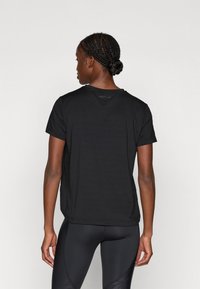 T-shirt noir à col rond et manches courtes, texture lisse et détail de logo subtil au dos. Coupe décontractée, associé à un legging noir.