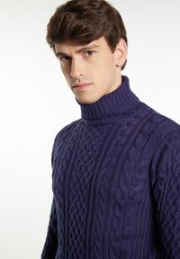 Pullover a collo alto in maglia con lavorazione a trecce di colore viola, caratterizzato da un motivo testurizzato e da un collo a coste. Il tessuto appare spesso e caldo.