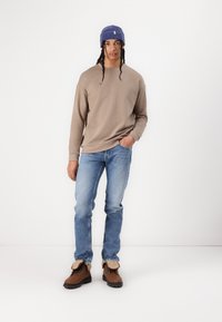 Bruine sweatshirt, lichtblauwe jeans en bruine laarzen met beige accenten. Blauwe gestreepte beanie. Glad materiaal, casual ontwerp, ontspannen pasvorm.