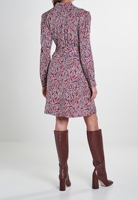 Abito a maniche lunghe con un motivo paisley rosso e blu. L'abito ha una silhouette aderente con un colletto a volant e un orlo sopra il ginocchio.