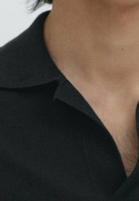 Zwarte poloshirt met een zachte textuur, klassieke kraag en een kleine inkeping bij de halslijn. Zichtbare huid onder de kraag.