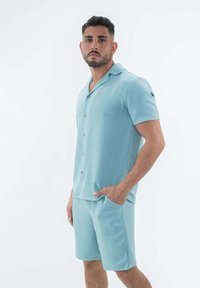 Chemise bleu clair à manches courtes avec un col ouvert et des boutons, assortie à un short comportant des poches latérales, fabriqué à partir d'un tissu texturé.
