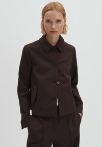 Bruine jas met een kraag, knoopsluiting aan de voorkant en twee zijzakken. Gemaakt van een glad, gestructureerd stof, met een getailleerde pasvorm.