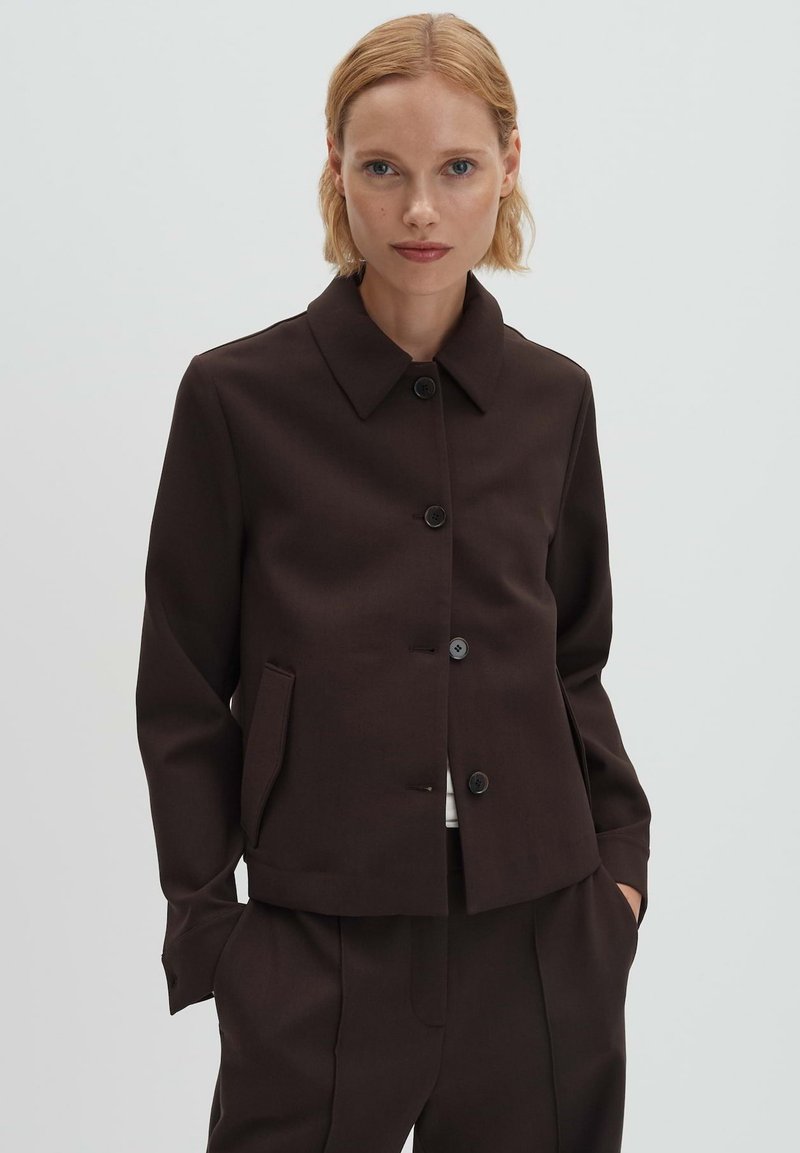 Bruine jas met een kraag, knoopsluiting aan de voorkant en twee zijzakken. Gemaakt van een glad, gestructureerd stof, met een getailleerde pasvorm.