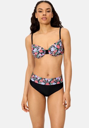 Mujer con un traje de baño de dos piezas, parte superior con estampado floral y parte inferior negra con una cinturilla floral a juego, de pie contra un fondo liso.