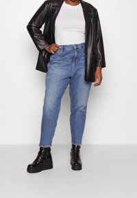 Svart läderblazer, vit t-shirt och högmidjade blå jeans. Svarta snörplattformsskor med tjock sula.