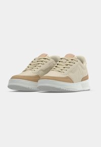 Baskets beige et tan avec un design bas, présentant une tige en suède texturé, des détails perforés et une semelle en caoutchouc blanche.