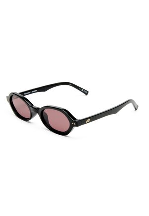 Gafas de sol ovaladas negras con lentes rojo oscuro y patillas finas, expuestas sobre un fondo blanco.