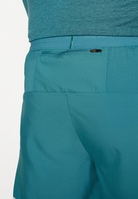 Teal idrottsshorts gjorda av mjukt, lätt material. Har en dragkedjeficka, texturerad midjeband och subtila perforeringar för ventilation.