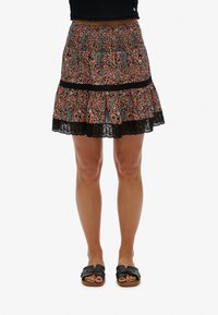 Sort og orange paisley-mønstret lagdelt miniskørt med smocket talje og blonder, parret med sorte slide sandaler.