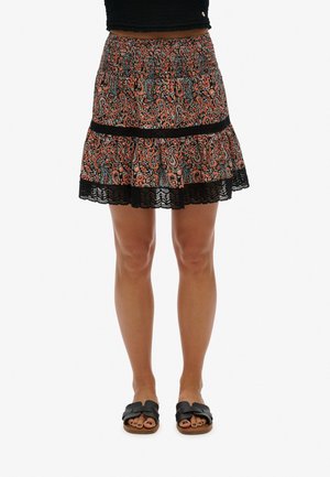 Jupe mini tiered en imprimé paisley noir et orange avec une taille smockée et une dentelle, assortie à des sandales à glissière noires.