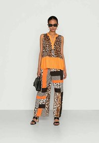 Blusa laranja com padrão de onça e bainha rodada, combinada com calças largas em patchwork que apresentam vários padrões de animais em tons de castanho e laranja.