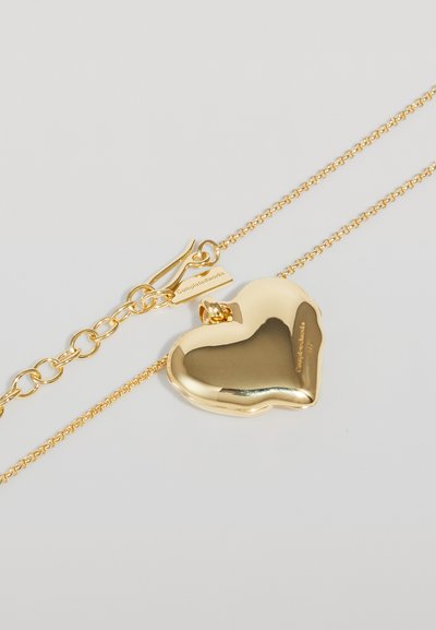 Collana con pendente a forma di cuore in oro, con una superficie liscia e riflettente; attaccata a una delicata catena con chiusura a gancio e dettaglio di branding.