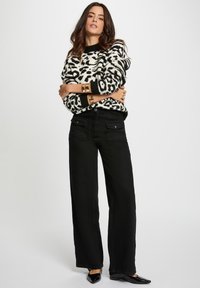 Pantaloni neri a gamba larga abbinati a un maglione crema con stampa leopardata nera. Gli accessori includono bracciali dorati. Un paio di scarpe nere semplici completano il look.