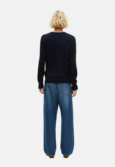 Marinepullover mit langen Ärmeln und geripptem Saum, kombiniert mit lockeren, hellblauen Jeans aus Denim mit Gesäßtaschen und sichtbaren Nähten.