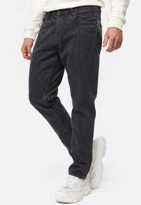 Vaqueros de mezclilla negra con un corte relajado, que presentan un clásico diseño de cinco bolsillos y detalles sutiles de desgastado, combinados con zapatillas blancas.