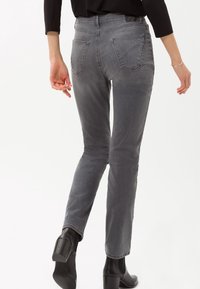 Vaqueros de mezclilla gris con un corte slim, que cuentan con bolsillos traseros y una cintura de altura media, combinados con botas de tacón negro hasta el tobillo.