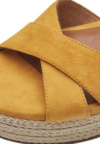 Sandalia de ante amarilla con correas cruzadas, que presenta una plataforma estilo espadrille texturizada con detalles trenzados y un forro interior suave.