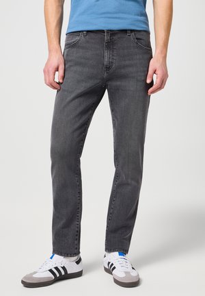 Jeans in denim grigio con vestibilità dritta, cinque tasche e una trama sottile, abbinati a sneakers bianche con strisce nere e dettagli blu.