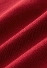 Tela de algodón roja con una textura suave y acanalada, que presenta ligeras ondulaciones y pliegues que enfatizan su calidad suave y elástica.
