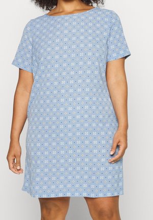 Femme portant une robe à manches courtes bleu clair avec un motif floral de marguerites blanches et jaunes.