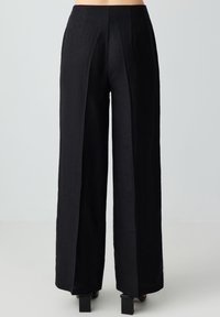 Pantaloni larghi neri realizzati in tessuto texturizzato, dotati di pieghe, vita alta e una vestibilità dritta che scende fino a terra.