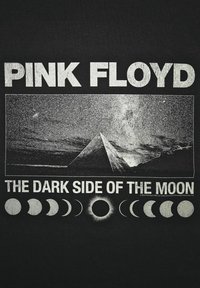 Černé tričko s nápisem "PINK FLOYD" tučným bílým písmem, obrázkem pyramidy a fázemi Měsíce pod "TMAVOU STRANOU MĚSÍCE."