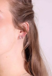 Deux boucles d'oreilles sur l'oreille d'un modèle : un anneau en argent et une fine bande ornée de pierres transparentes, mettant en valeur une finition métallique et des textures lisses.