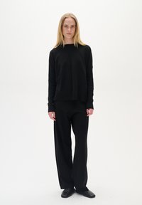 Schwarzer Strickpullover und weite Hosen, bestehend aus langen Ärmeln, lockerem Schnitt und nahtlosem Design; getragen mit schlichten schwarzen Schuhen.